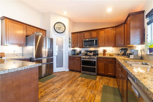 kitchen with sink, dark wood-type flooring, appliances with stainless steel finishes, light stone countertops, and vaulted ceiling