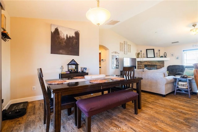 dining area featuring a fireplace, hardwood / wood-style flooring, and vaulted ceiling