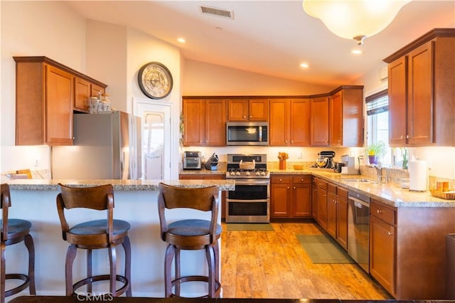 kitchen featuring lofted ceiling, sink, a kitchen breakfast bar, light stone counters, and stainless steel appliances