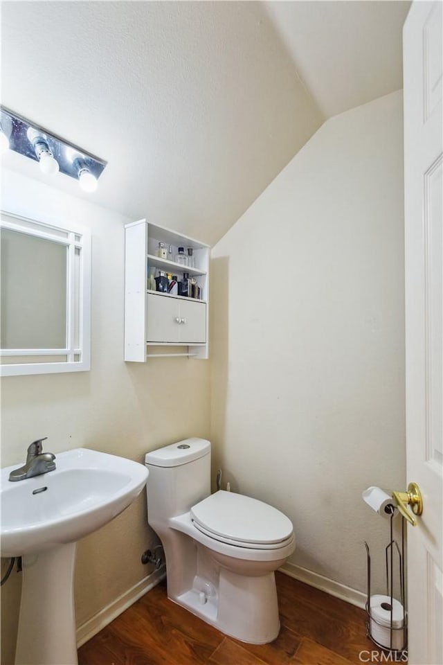 bathroom featuring hardwood / wood-style floors, vaulted ceiling, sink, and toilet