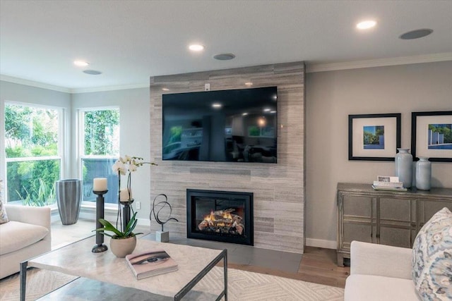 living room with a tiled fireplace, ornamental molding, and light hardwood / wood-style flooring