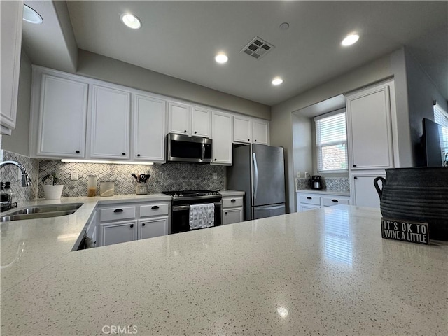 kitchen with tasteful backsplash, sink, white cabinets, stainless steel appliances, and light stone countertops