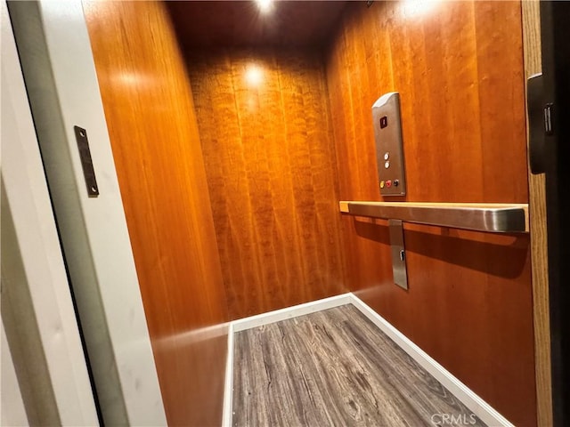 room details with hardwood / wood-style floors, elevator, and wooden walls