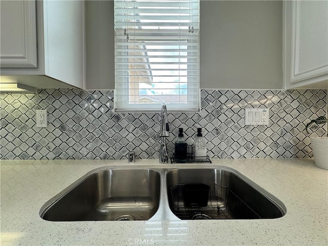 kitchen with light stone counters, white cabinets, sink, and backsplash