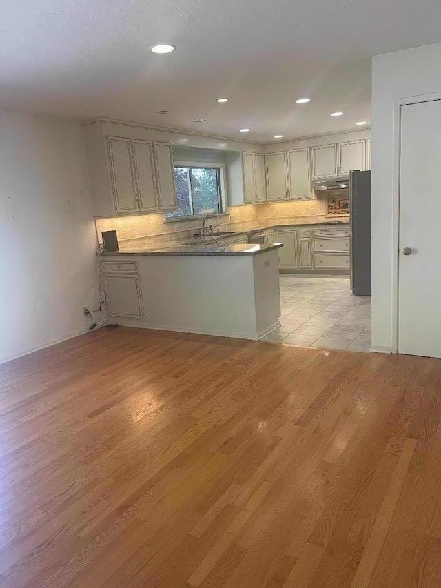 kitchen featuring sink, tasteful backsplash, light hardwood / wood-style flooring, fridge, and kitchen peninsula