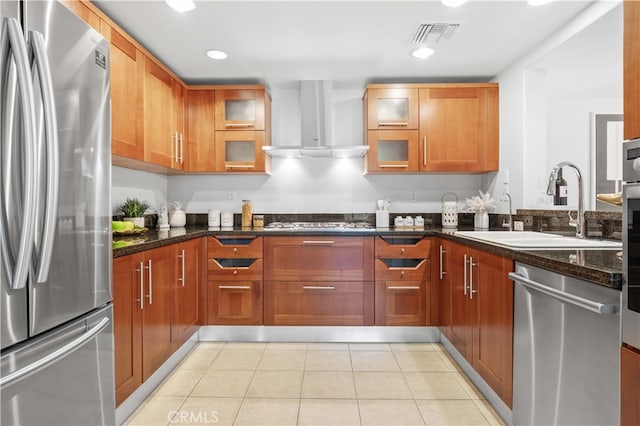 kitchen with appliances with stainless steel finishes, sink, dark stone counters, light tile patterned floors, and wall chimney range hood