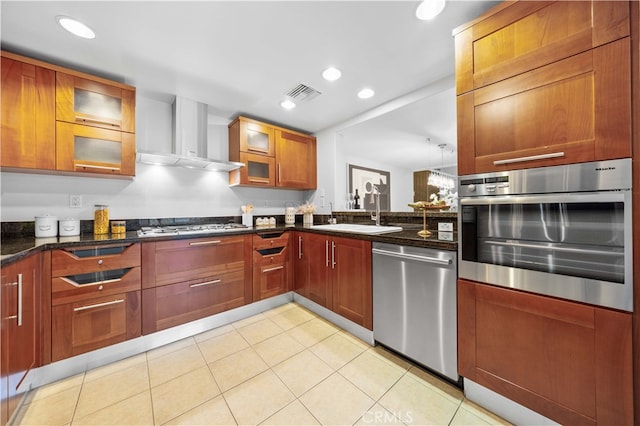 kitchen with sink, wall chimney range hood, appliances with stainless steel finishes, dark stone countertops, and light tile patterned flooring