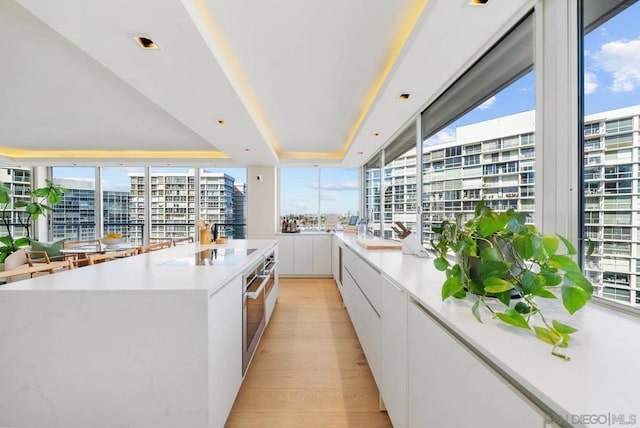 kitchen featuring white cabinets, black electric cooktop, a large island, a tray ceiling, and light wood-type flooring