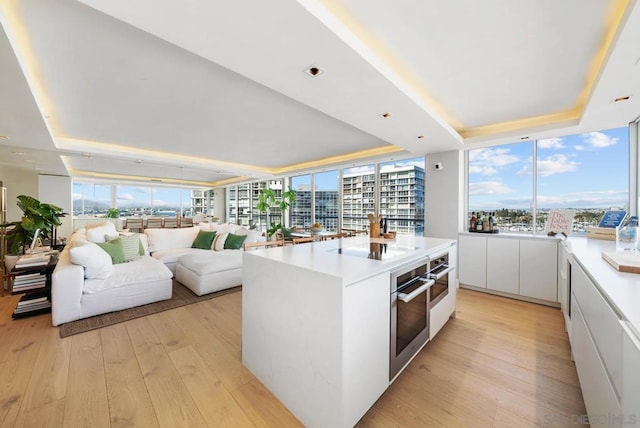 kitchen featuring oven, light hardwood / wood-style flooring, white cabinets, and a tray ceiling