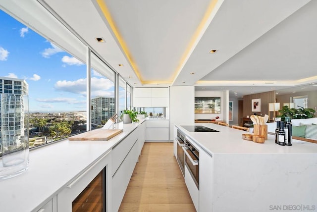 kitchen with a raised ceiling, wine cooler, white cabinets, and light hardwood / wood-style flooring