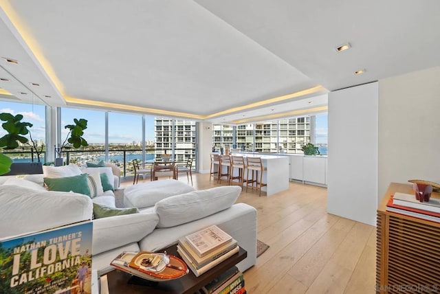 living room with a tray ceiling, a wall of windows, and light wood-type flooring