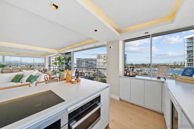 kitchen with plenty of natural light, white cabinets, light wood-type flooring, and a tray ceiling