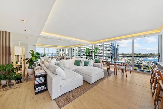 living room featuring floor to ceiling windows, light hardwood / wood-style flooring, a raised ceiling, and a water view