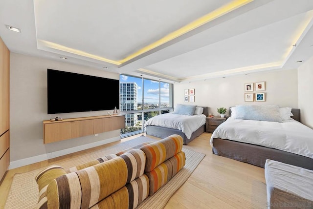 bedroom featuring floor to ceiling windows, a raised ceiling, and light hardwood / wood-style floors