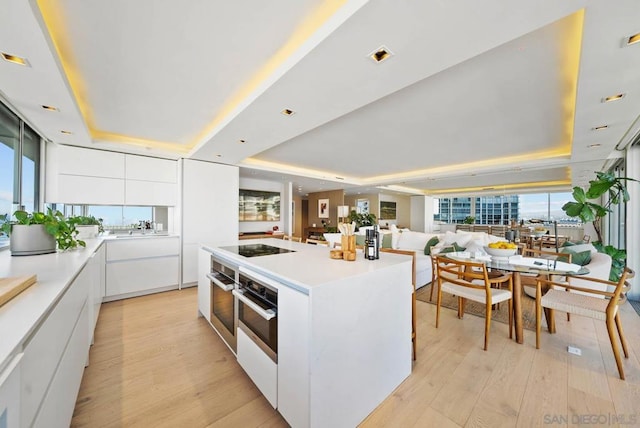 kitchen with a raised ceiling, white cabinetry, a kitchen island, and light hardwood / wood-style floors