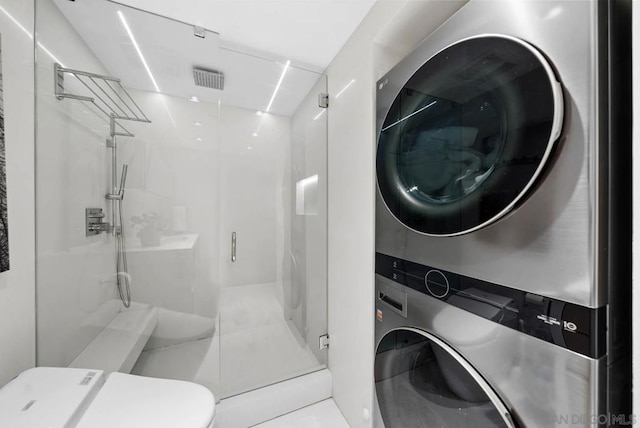 bathroom featuring stacked washer and dryer, a shower with door, and toilet