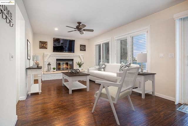 living room with a brick fireplace, dark wood-type flooring, and ceiling fan