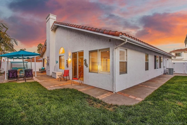 back house at dusk with a yard, central AC, and a patio