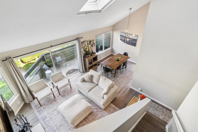 living room with high vaulted ceiling, a skylight, hardwood / wood-style floors, and a notable chandelier