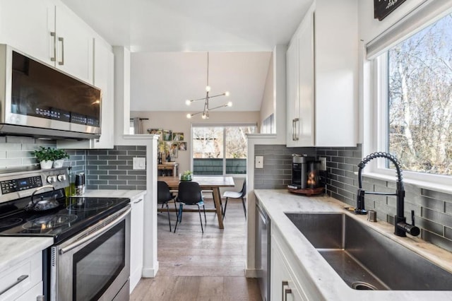 kitchen with appliances with stainless steel finishes, lofted ceiling, sink, white cabinets, and light stone counters