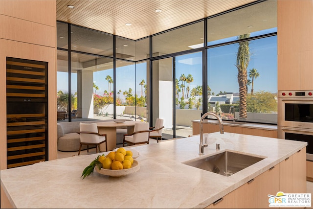 kitchen featuring sink, a wall of windows, light stone countertops, light brown cabinetry, and stainless steel double oven