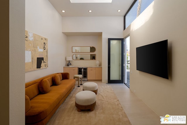 living room with wine cooler, a skylight, light hardwood / wood-style flooring, and a high ceiling