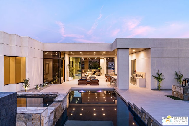 patio terrace at dusk with a pool with hot tub, an outdoor living space, and exterior kitchen