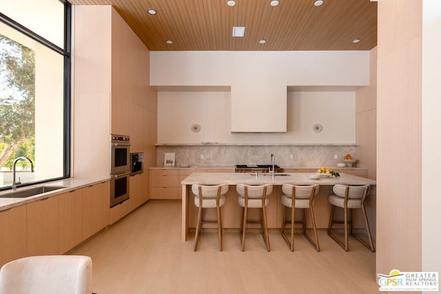 kitchen featuring decorative backsplash, a kitchen island with sink, sink, and a breakfast bar area