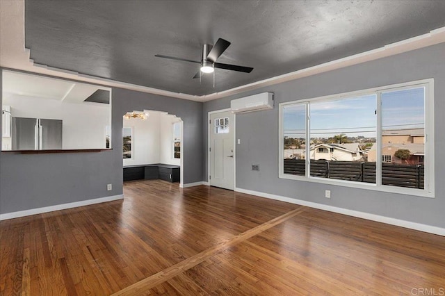 unfurnished living room with hardwood / wood-style floors, ceiling fan with notable chandelier, and a wall unit AC