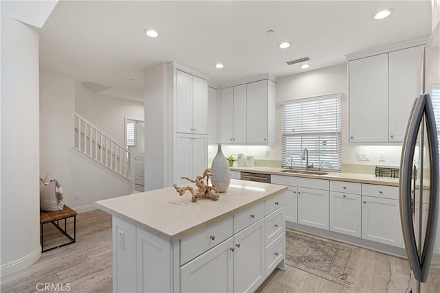 kitchen featuring sink, a center island, fridge, light hardwood / wood-style floors, and white cabinets