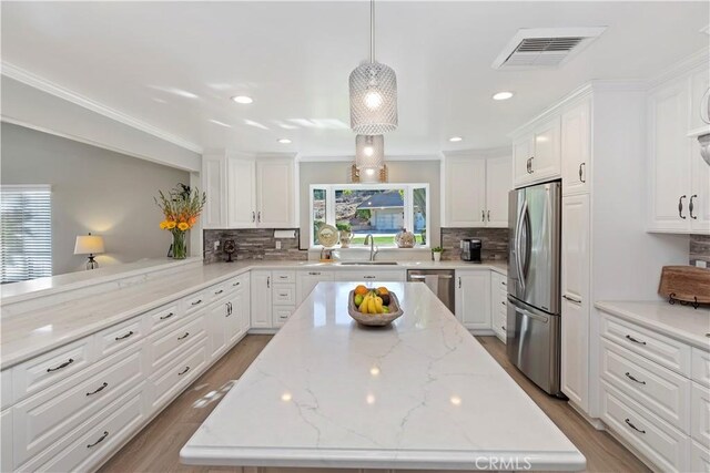 kitchen with appliances with stainless steel finishes, sink, white cabinets, hanging light fixtures, and light stone counters