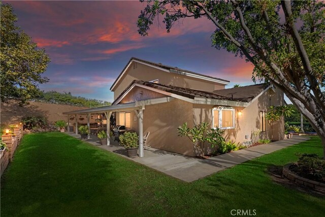 back house at dusk featuring a yard and a patio