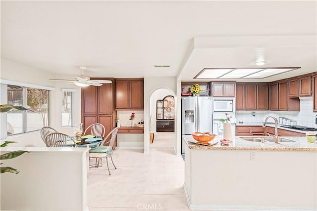 kitchen featuring sink, stainless steel fridge, light stone countertops, white microwave, and decorative backsplash