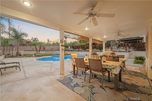 patio terrace at dusk with ceiling fan and a fenced in pool