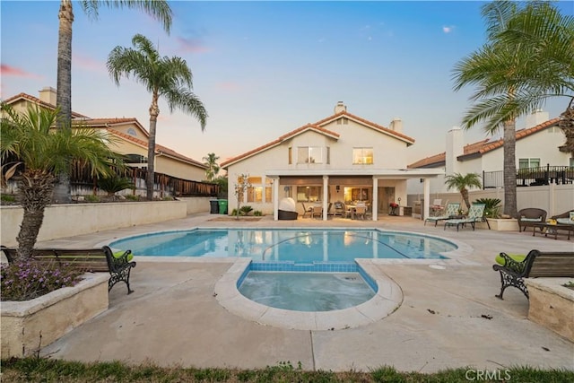 pool at dusk featuring an in ground hot tub and a patio area