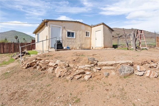 rear view of property with fence, a mountain view, and stucco siding