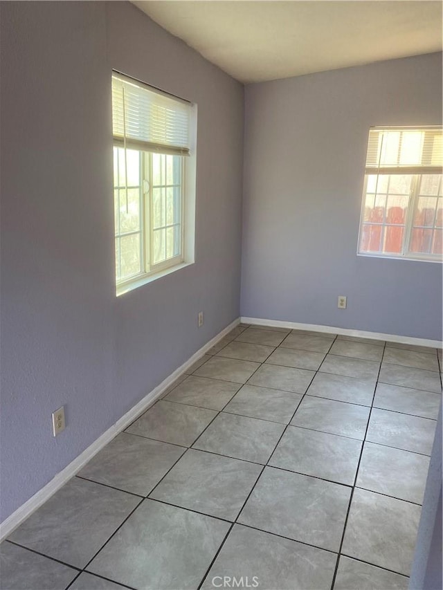 empty room featuring light tile patterned floors, plenty of natural light, and baseboards