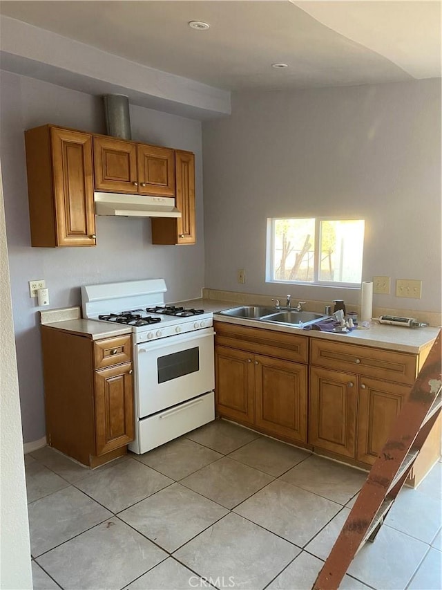 kitchen with brown cabinets, light tile patterned floors, light countertops, white range with gas stovetop, and under cabinet range hood