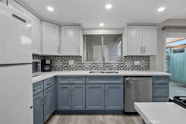 kitchen with appliances with stainless steel finishes, sink, light wood-type flooring, and decorative backsplash