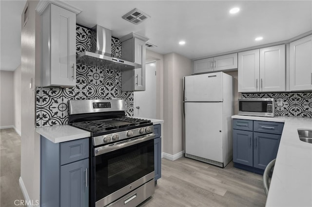 kitchen with stainless steel appliances, decorative backsplash, light wood-type flooring, and wall chimney exhaust hood