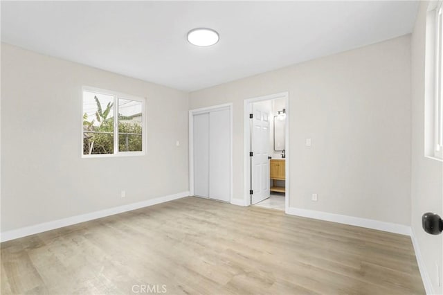 unfurnished bedroom featuring ensuite bathroom, a closet, and light hardwood / wood-style flooring