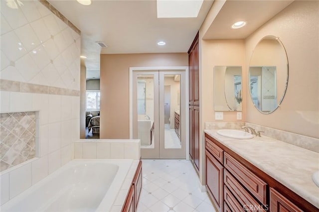 bathroom featuring a skylight, vanity, a relaxing tiled tub, and french doors