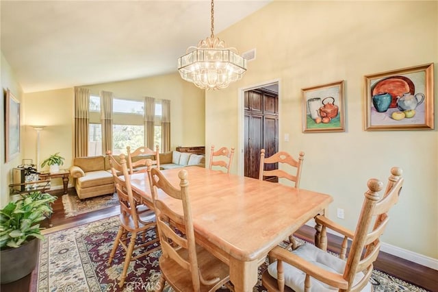 dining space with an inviting chandelier, dark wood-type flooring, and vaulted ceiling