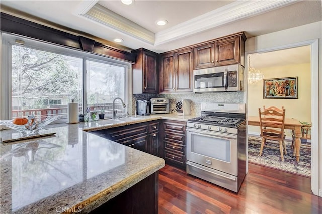 kitchen featuring appliances with stainless steel finishes, dark hardwood / wood-style floors, backsplash, a raised ceiling, and light stone countertops