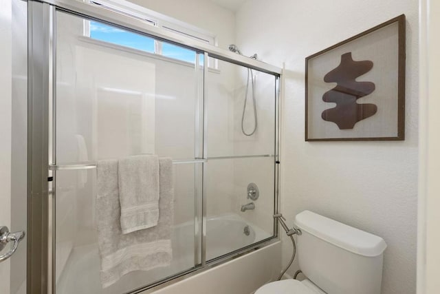 bathroom featuring toilet and bath / shower combo with glass door