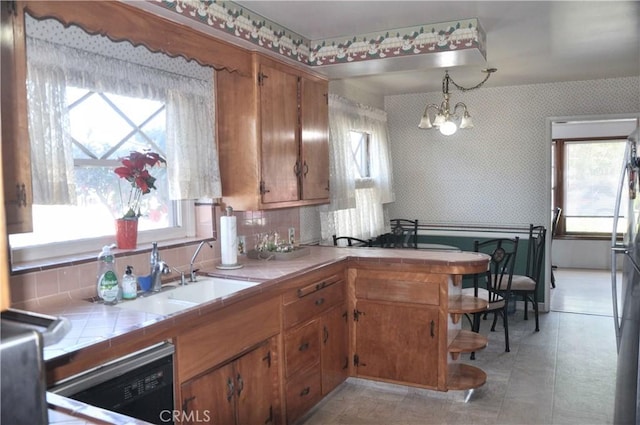 kitchen with pendant lighting, sink, black dishwasher, tile countertops, and a chandelier