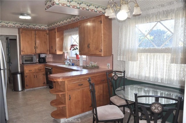 kitchen featuring pendant lighting, tile countertops, sink, a notable chandelier, and kitchen peninsula