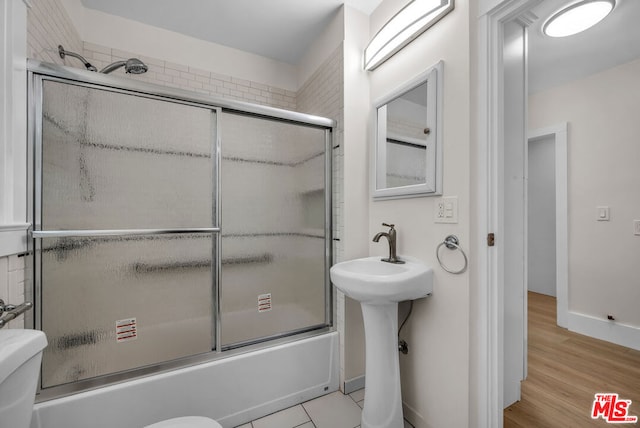 full bathroom featuring hardwood / wood-style flooring, sink, shower / bath combination with glass door, and toilet