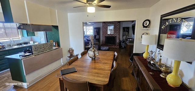 dining space with a fireplace, dark wood-type flooring, sink, and ceiling fan