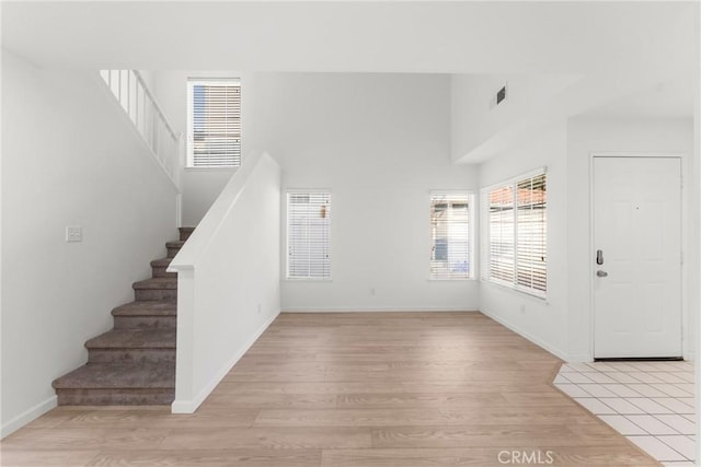 foyer entrance featuring a towering ceiling and light wood-type flooring